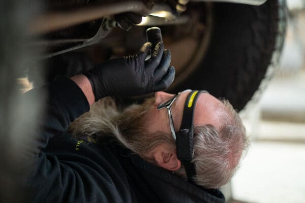 10 mil Pure Nitrile Gloves with Extended Cuff being used in an automotive shop. Mechanic under the van, inspecting with a flashlight